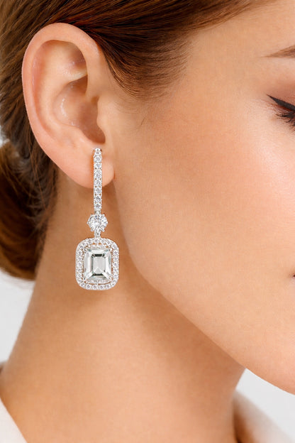 Emerald cut halo drop earrings worn on ear with white gold finish